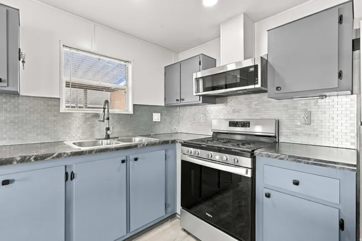 Kitchen featuring stainless steel appliances, a double basin sink, mosaic tile backsplash, and two-tone cabinetry