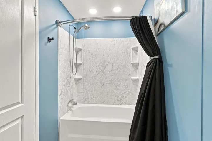 Tub/shower combination featuring a curved shower rod, built-in shelving, and a chrome shower head with handheld attachment