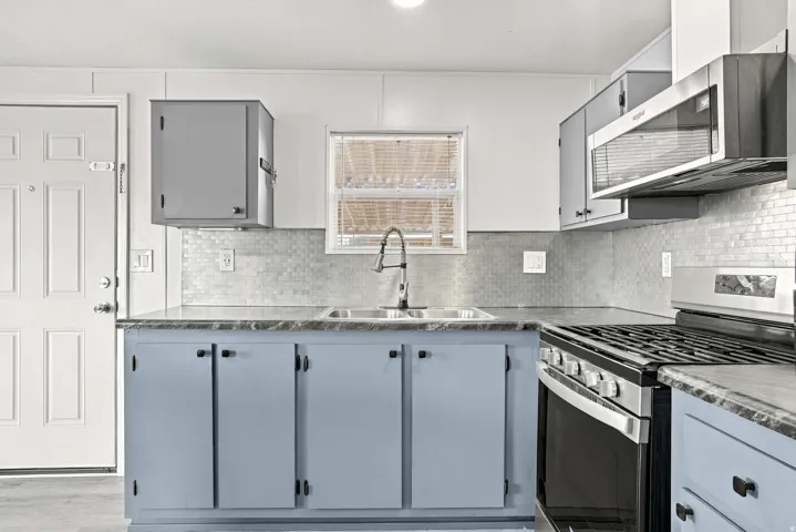 Kitchen featuring a dual basin stainless steel sink, tile backsplash, built-in microwave, and a gas range