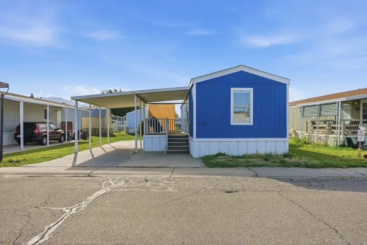Blue exterior siding with white trim, covered carport, front porch with steps, white skirting, and an awning over the entrance