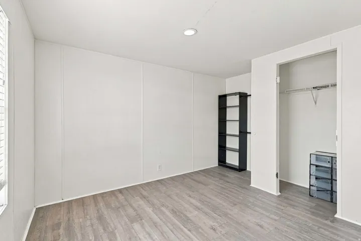 Wood-finish flooring, recessed lighting, and a built-in closet with shelving and hanging rod