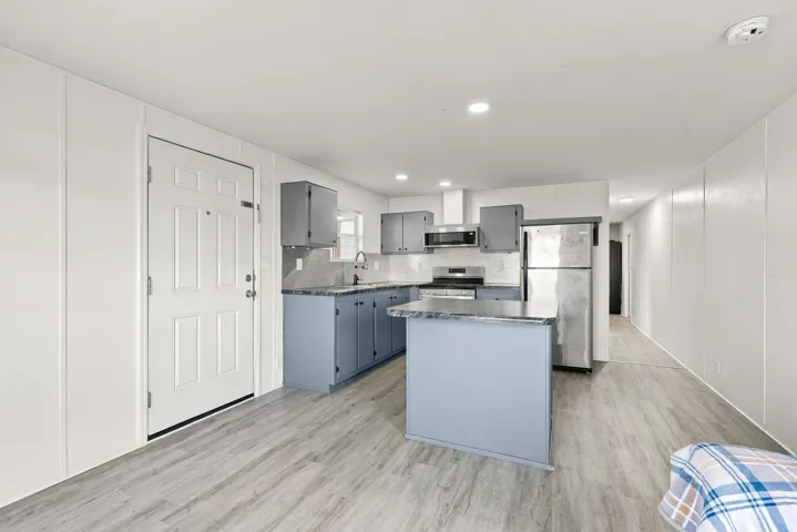 Open-concept kitchen with light gray cabinetry, stainless steel appliances, a center island, and wood-finish flooring