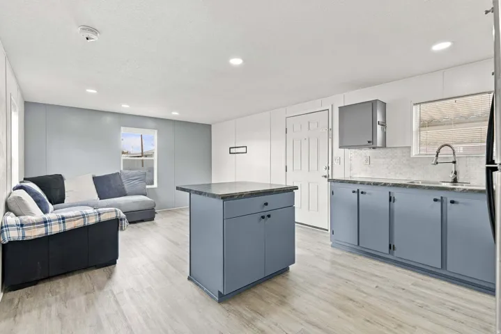 Kitchen featuring blue cabinetry, light-toned wood-finish flooring, recessed lighting, a kitchen island, and a tile backsplash