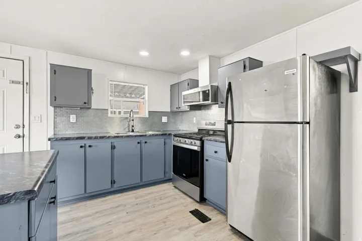 Kitchen featuring gray cabinetry, composite countertops, stainless steel appliances, a tiled backsplash, and wood-finish flooring