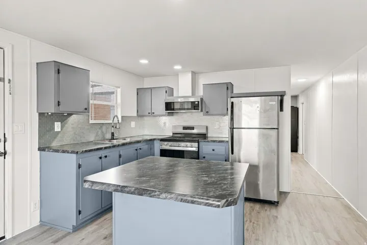 Kitchen featuring stainless steel appliances, a central island, grey cabinetry, and wood-finish flooring