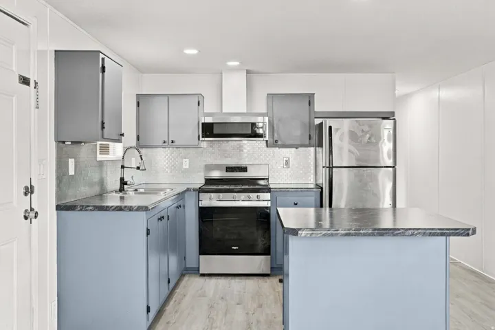 Kitchen featuring stainless steel appliances, a tile backsplash, wood-finish flooring, a kitchen island, and upper and lower cabinetry
