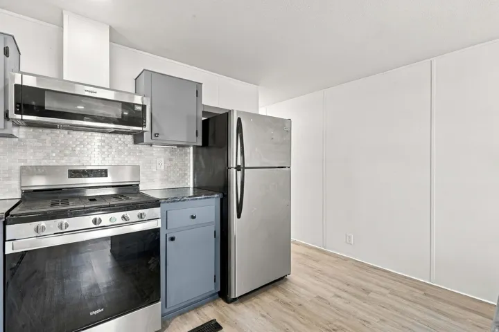 Stainless steel appliances, over-range microwave, gray cabinetry, tile backsplash, and light wood-finish flooring