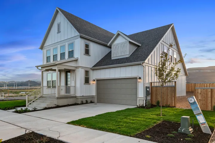 Modern farmhouse exterior with board and batten siding, a covered front porch, an attached garage, a paved driveway, and manicured landscaping