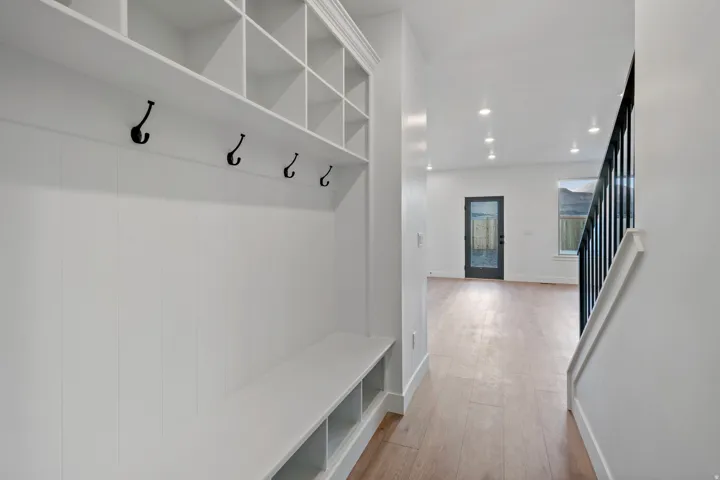 Built-in cubby storage with bench seating and coat hooks, wood-finish flooring, recessed lighting, and a modern stair railing