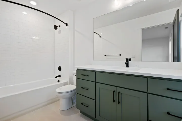 Built-in vanity with a composite countertop and integrated sink, matte black hardware, and a tub with subway tile surround