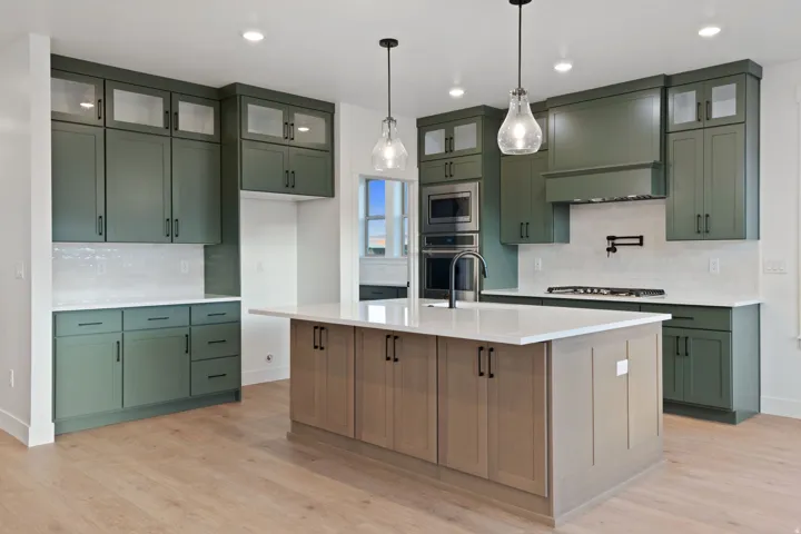 Kitchen featuring green cabinetry, light wood-finish flooring, a central island with a white countertop, built-in ovens, and a gas range