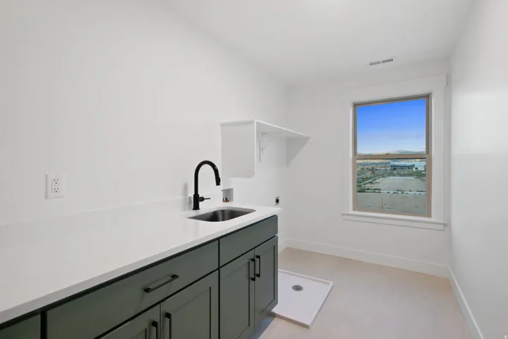 Laundry room featuring white walls, a single window, a white countertop, a dark green cabinetry, and a stainless steel sink with a black faucet