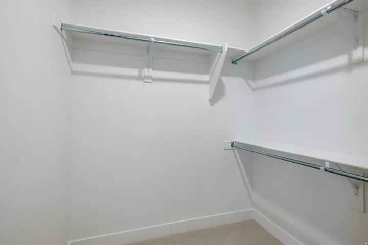 Walk-in closet with multiple white shelving units, chrome hanging rods, and neutral carpet