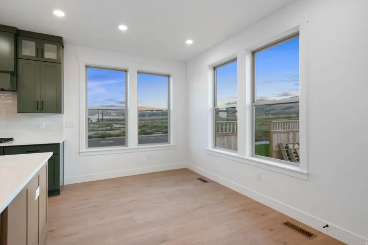 Recessed lighting, wood-finish flooring, white walls, multiple windows, and dark green cabinetry