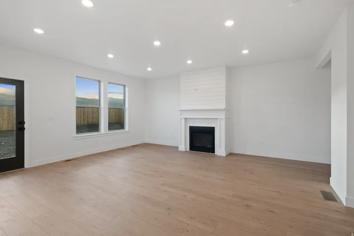 Recessed lighting, wood-finish flooring, white walls, black framed glass door, and a built-in fireplace with a white mantel and shiplap accent