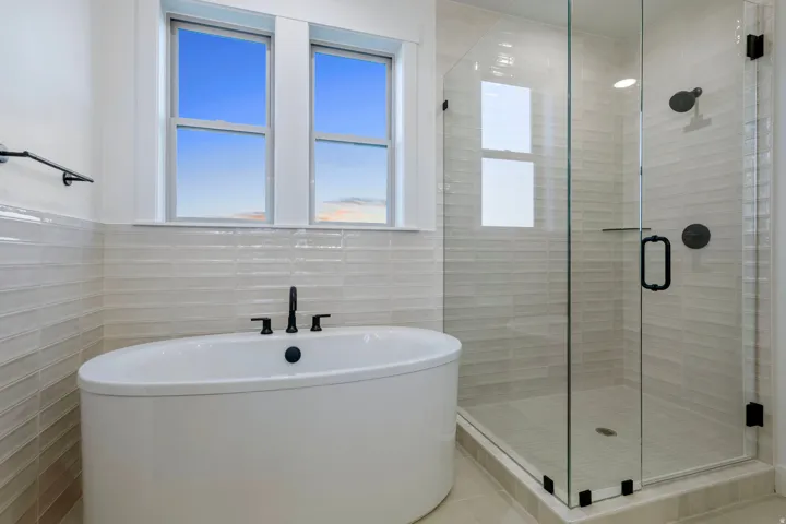 Freestanding oval soaking tub with matte black fixtures, glass-enclosed shower, and tiled walls