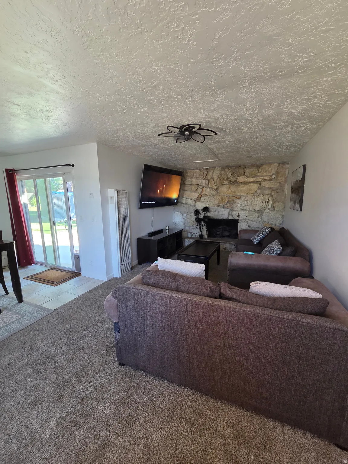Living area featuring a stone-faced fireplace, ceiling fan, and carpeted flooring