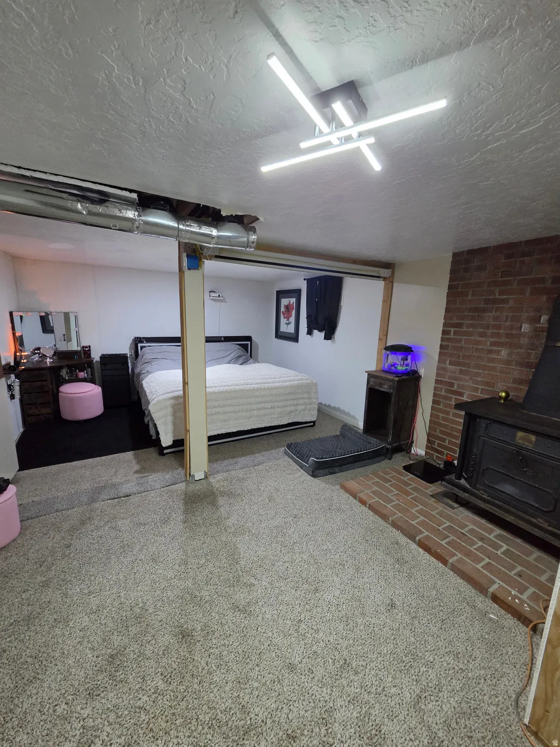 Brick hearth with a wood-burning stove, exposed ductwork, carpet flooring, and a modern ceiling light fixture
