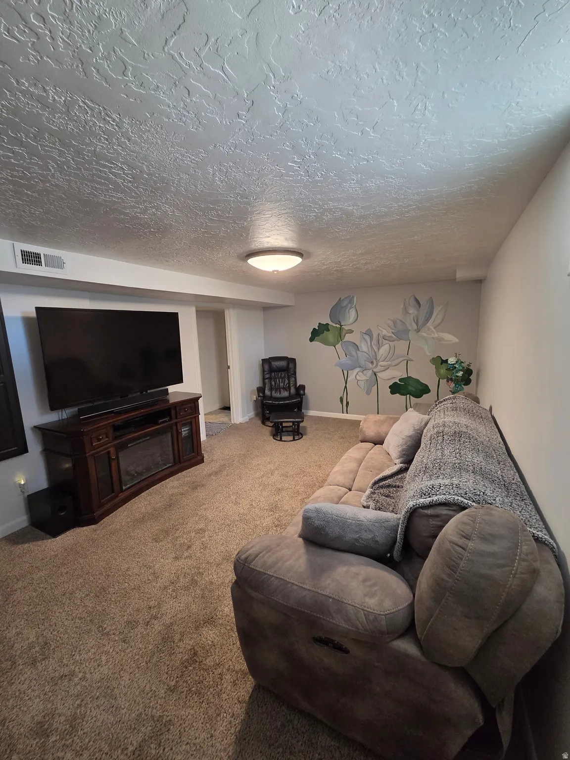 Carpeted living area featuring a decorative wall mural, recessed lighting, and a built-in media console with an electric fireplace