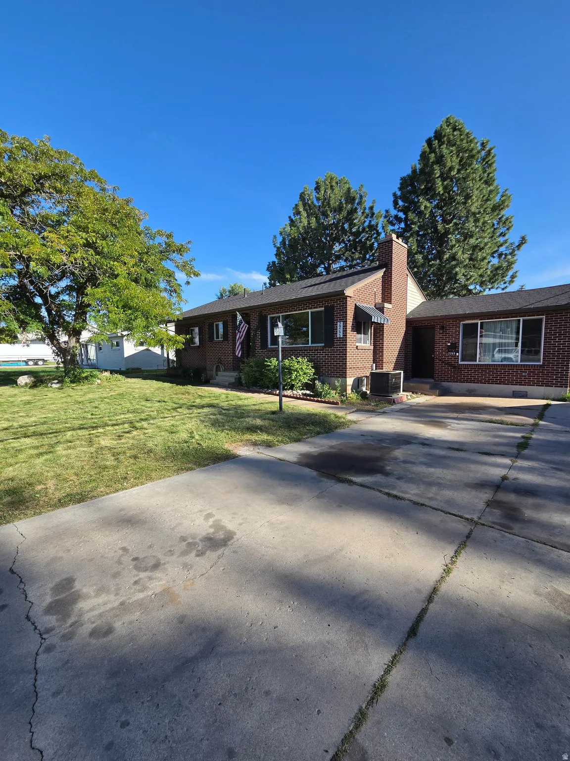 Brick exterior with a prominent chimney, dark-shingled roof, and a concrete driveway