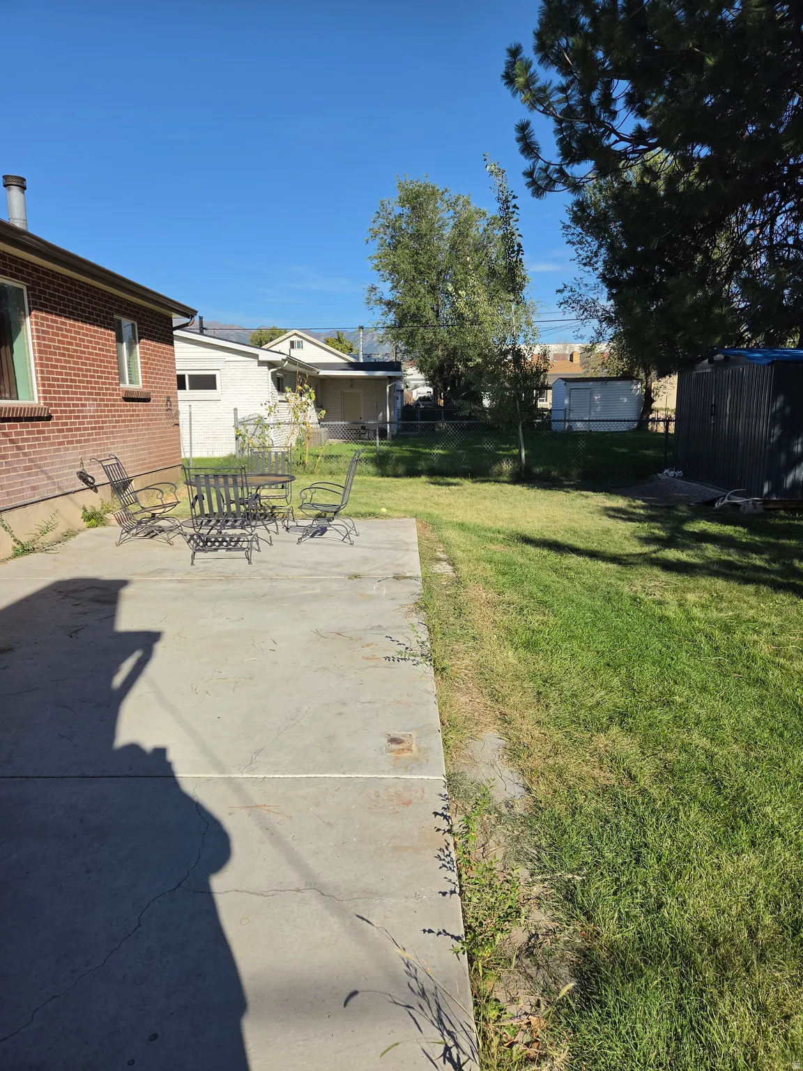 Rear brick exterior with a concrete patio, expansive lawn, and mature trees