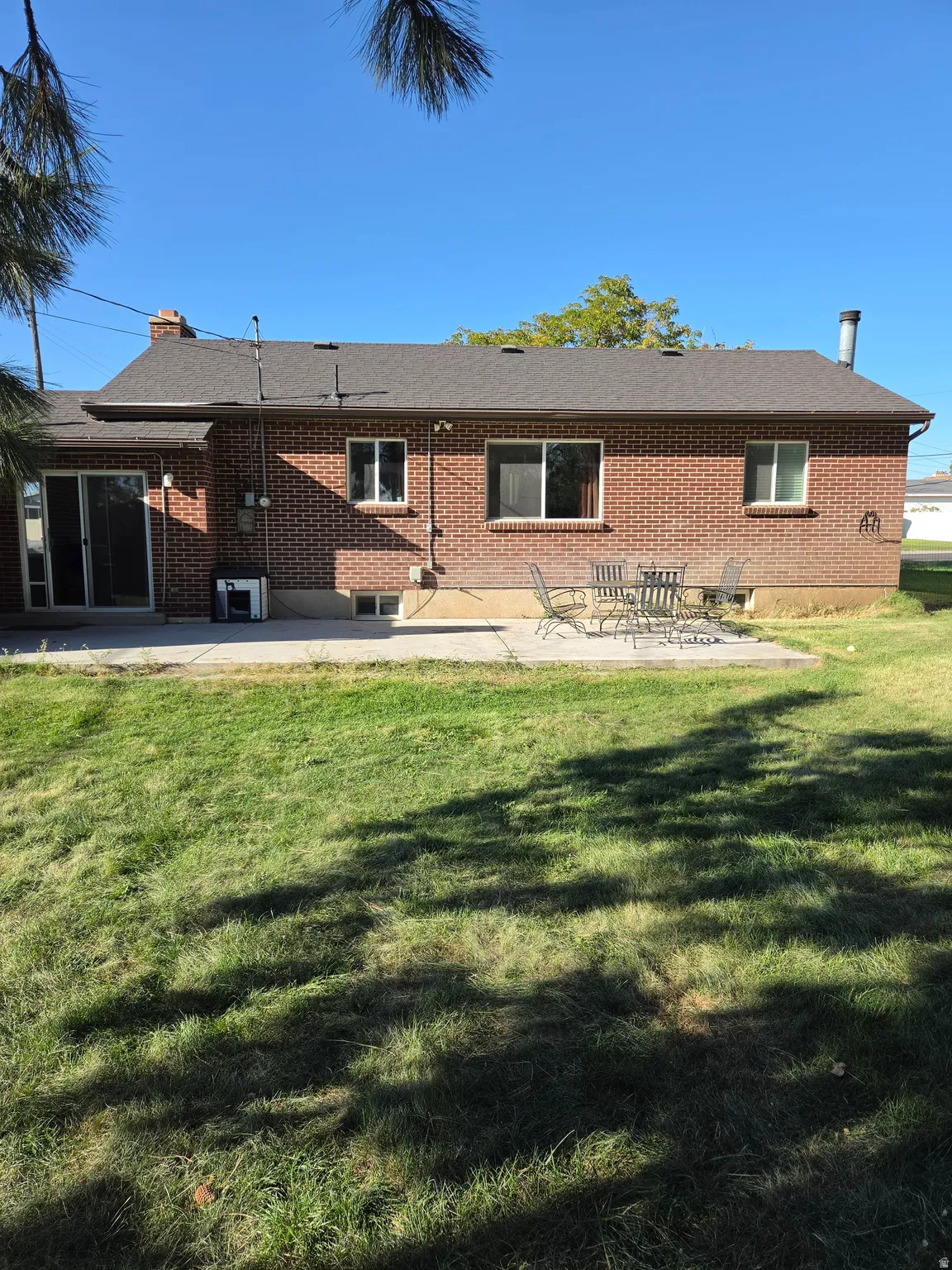 Brick exterior with a shingled roof, a concrete patio, and a sliding glass door