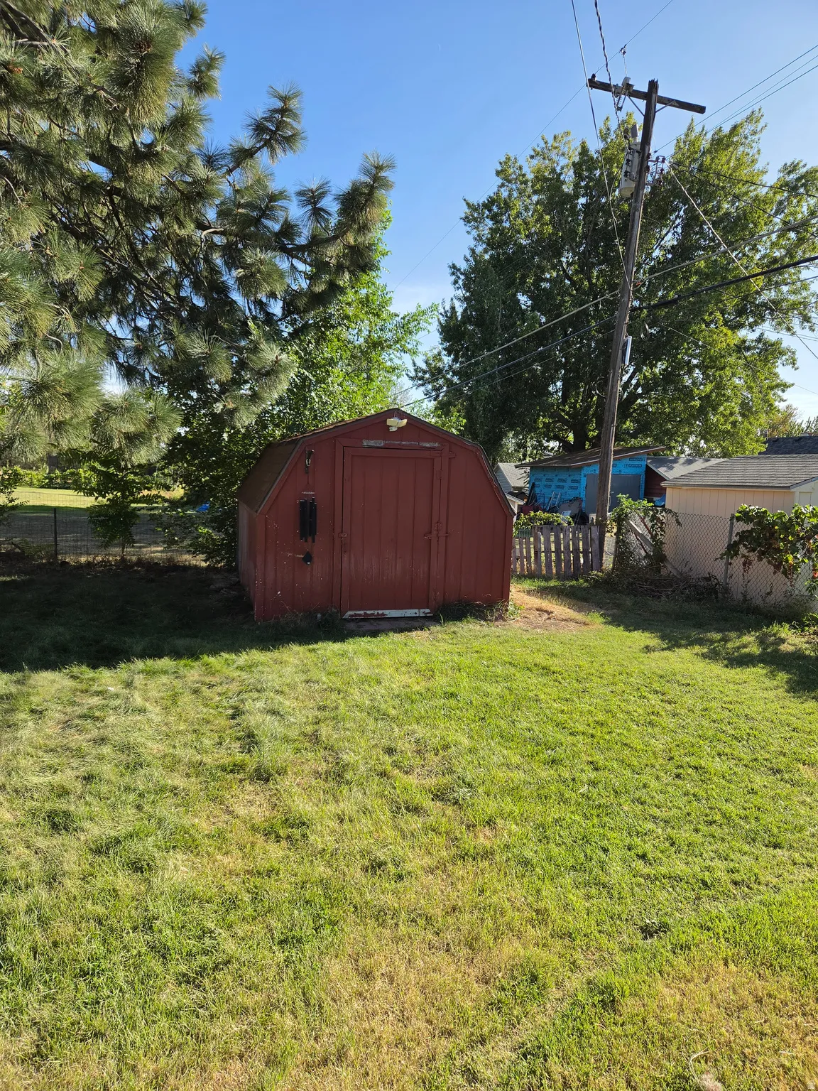 Red barn-style shed with a single door, situated on a grassy area