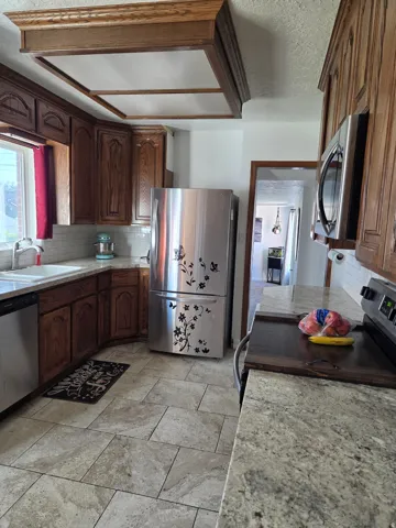 Kitchen featuring wood cabinetry, stainless steel appliances, light-toned tile flooring, and granite counter tops