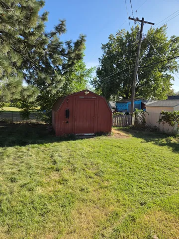 Red barn-style shed with a single door, situated on a grassy area