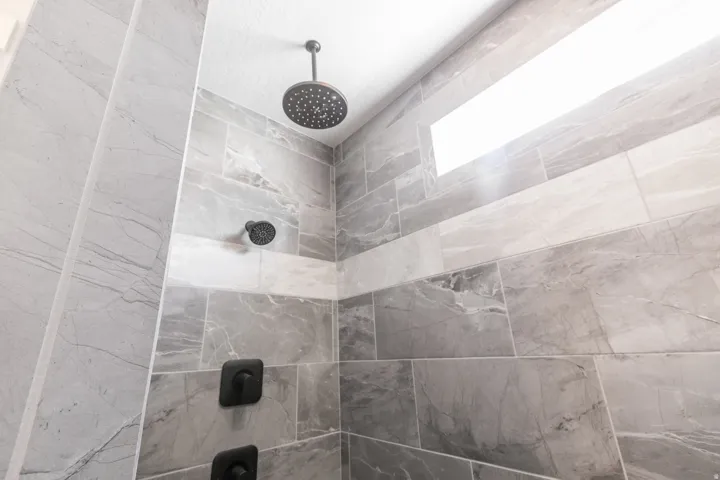 Shower enclosure featuring ceiling-mounted rain showerhead, wall-mounted showerhead, and matte black fixtures