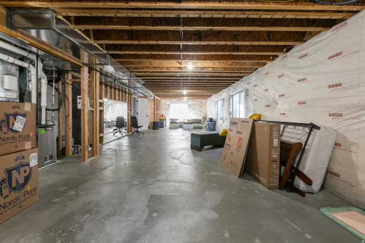 Unfinished basement with concrete flooring, exposed wood joists, utility systems, and framed interior walls