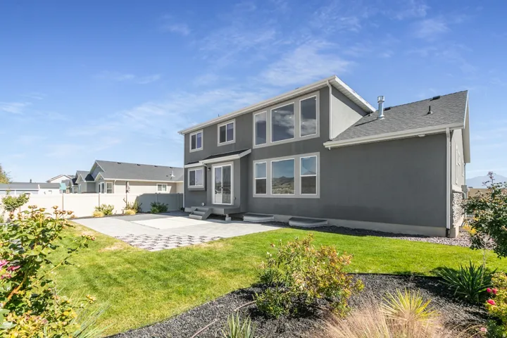 Expansive rear exterior with a multi-level design, featuring large windows, a ground-level patio, and a well-maintained lawn