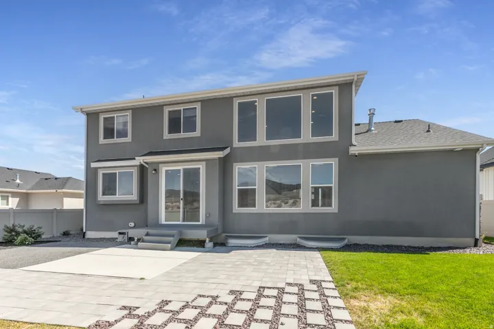 Gray stucco exterior with multiple windows, a sliding glass door, and a tiled patio with integrated gravel