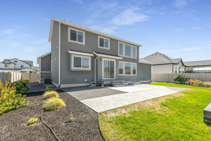 Rear exterior featuring a stone patio, manicured lawn, and sliding glass door