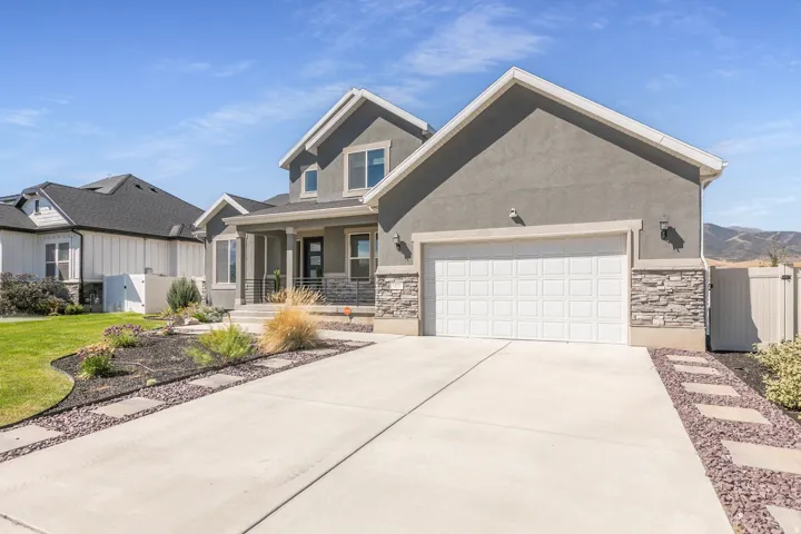 Stucco exterior with stone accents, covered front porch, integrated garage, concrete driveway, and landscaped front yard