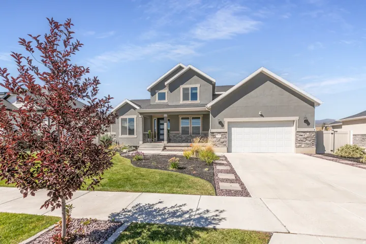 Gray stucco exterior with stacked stone accents, a covered front porch, and an attached two-car garage