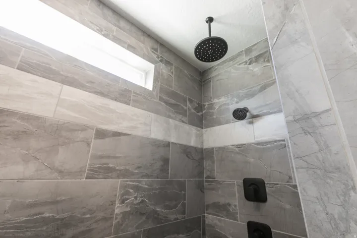 Tiled shower with a rain shower head, additional shower head, matte black fixtures, and a high horizontal window