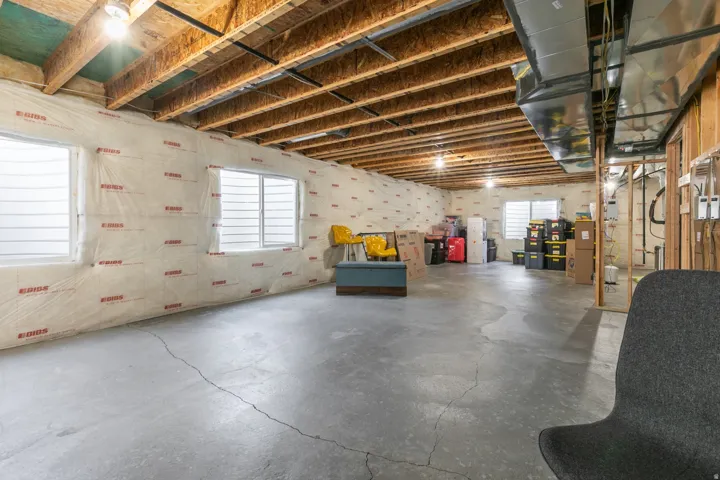 Unfinished basement featuring exposed ceiling joists, multiple windows, concrete flooring, and visible HVAC ductwork