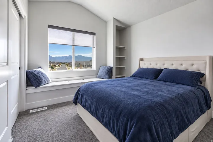 Vaulted ceiling with built-in shelving, window with mountain backdrop, window seat, and carpeted flooring