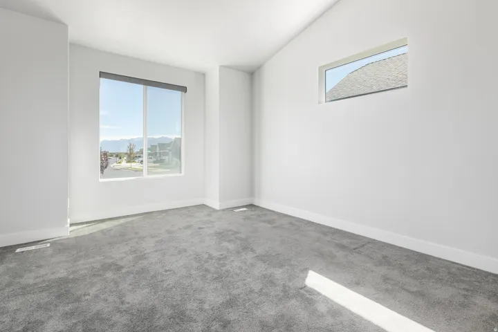 Carpeted room featuring a large window with a roller shade, an additional transom window, and a sloped ceiling