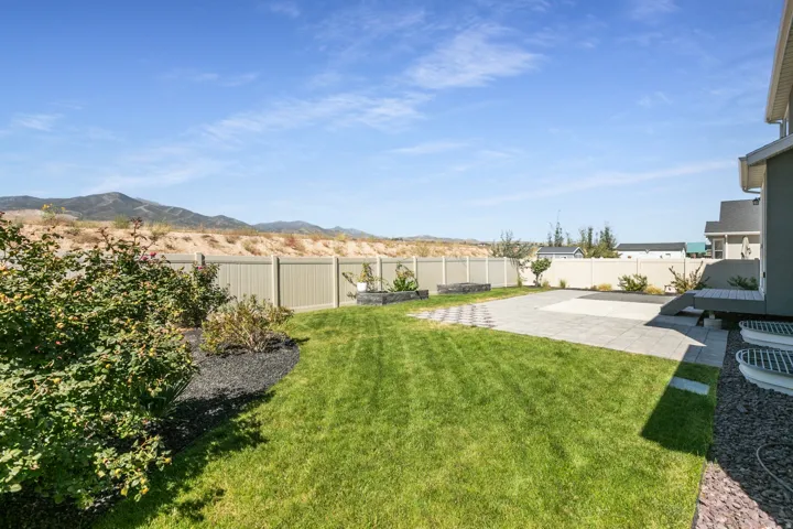 Expansive backyard featuring a paver patio, manicured lawn, dedicated garden beds, and mature landscaping
