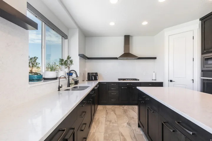 Kitchen featuring dark wood-finish cabinetry, light-toned countertops, a stainless steel range hood, built-in appliances, and recessed lighting