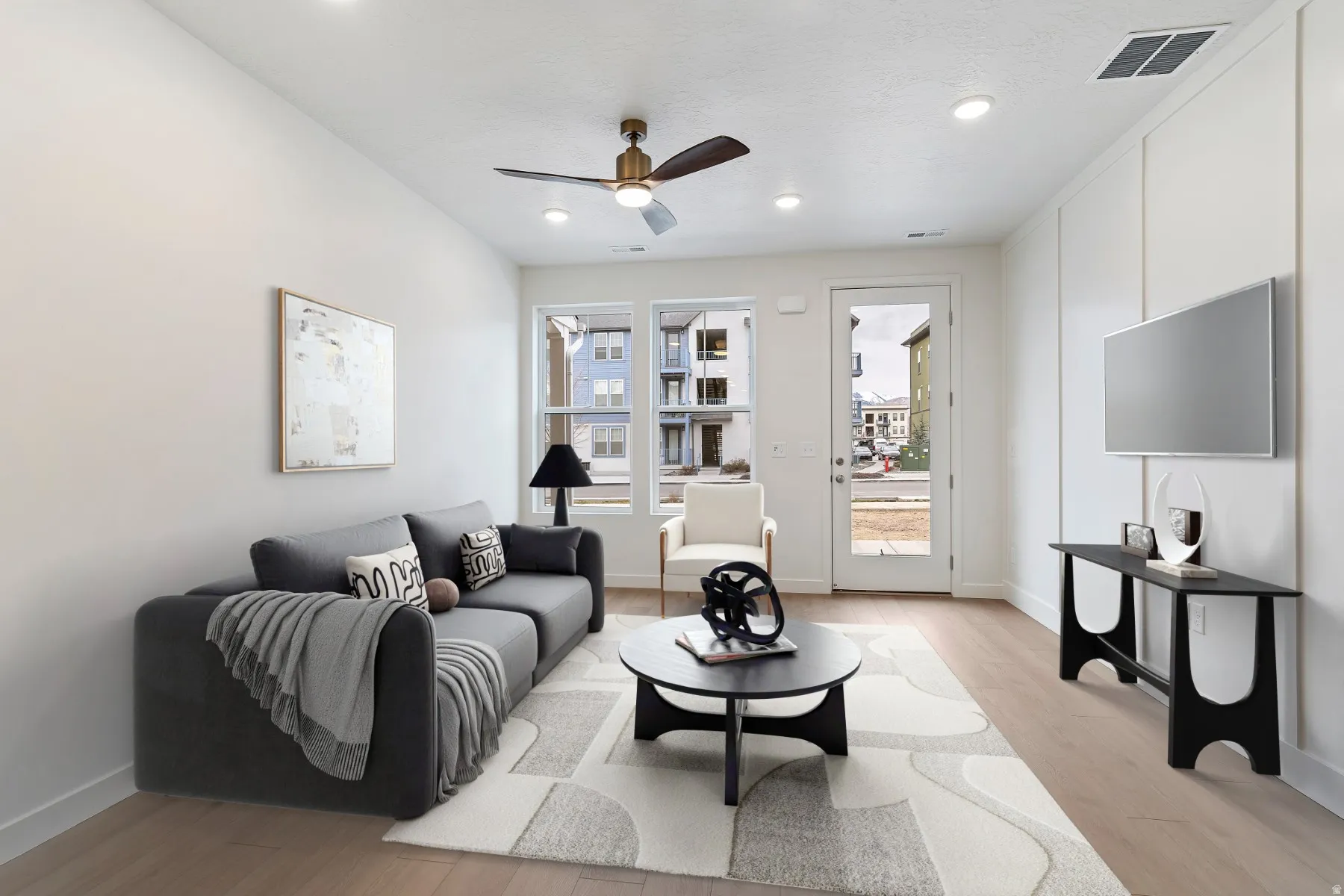 Recessed lighting and ceiling fan, light wood-finish flooring, white panel accent wall, and a glass-paneled door