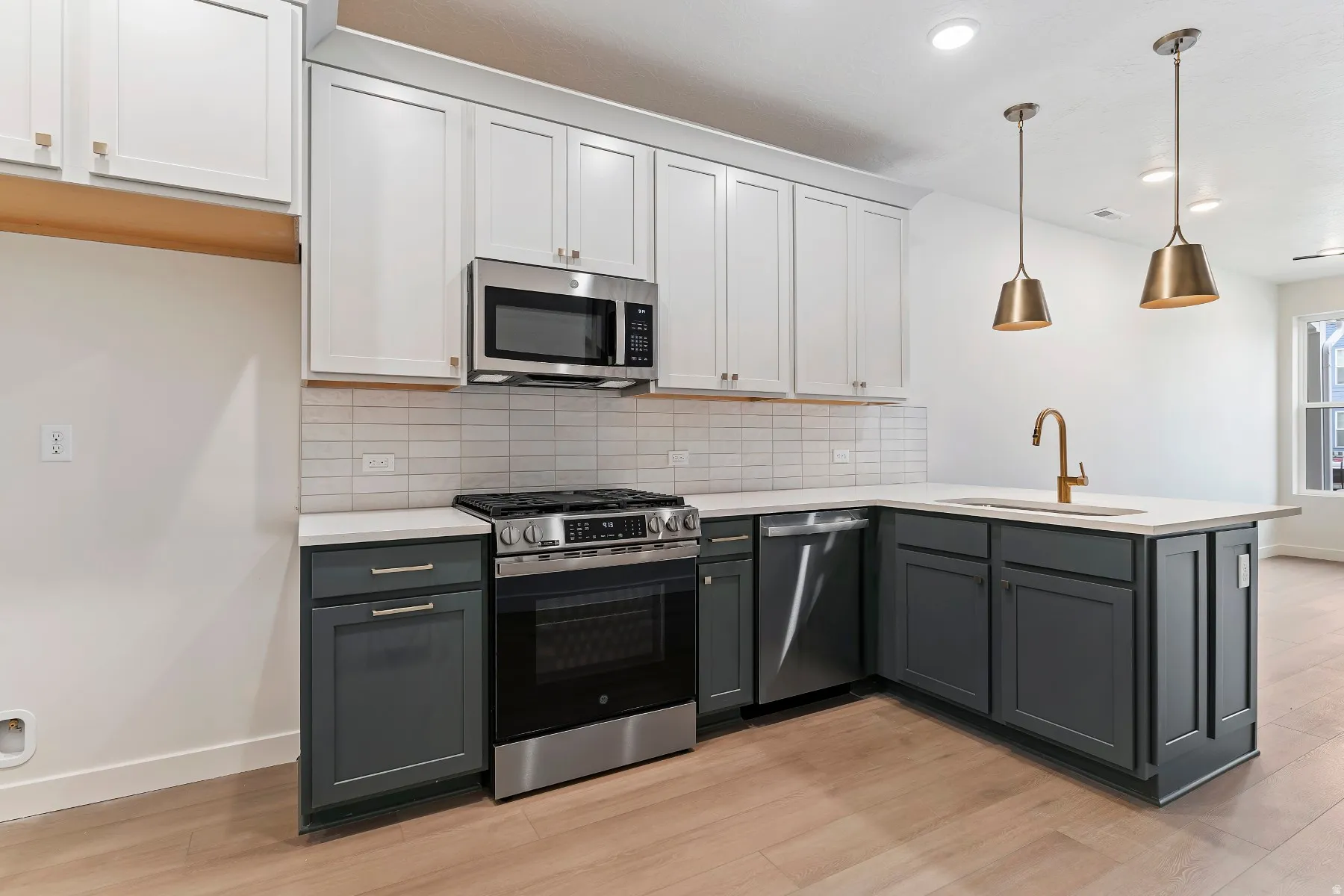 Kitchen featuring a white and dark gray cabinetry, stainless steel appliances, light-colored countertops, tile backsplash, and wood-finish flooring