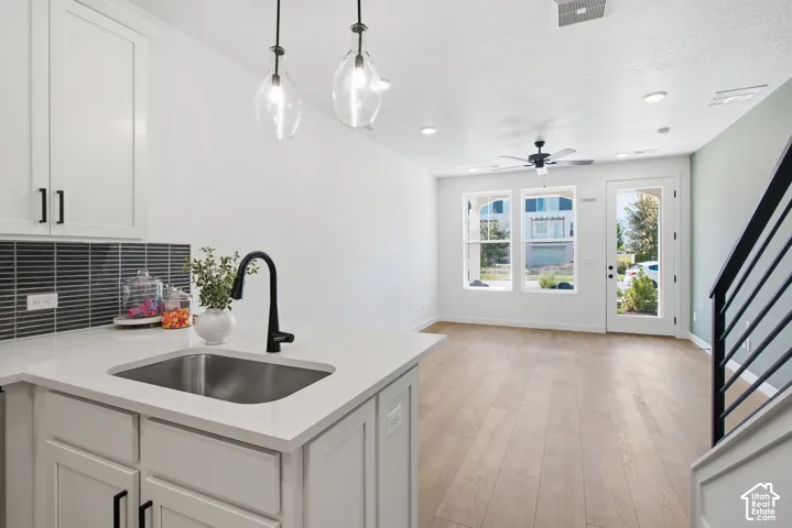 Modern kitchen sink with a matte black gooseneck faucet, white shaker cabinetry, tiled backsplash, and recessed lighting