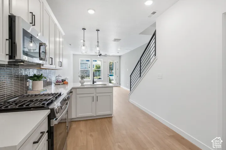 Modern kitchen featuring white cabinetry, stainless steel appliances, a mosaic tile backsplash, and light wood-finish flooring