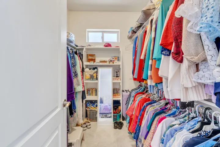 Primary suite walk-in closet featuring white built-in shelving, hanging rods, and a high-set window