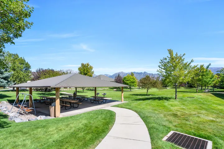Expansive green space featuring a covered pavilion with picnic tables, a designated grill area, a swing set, and mature trees