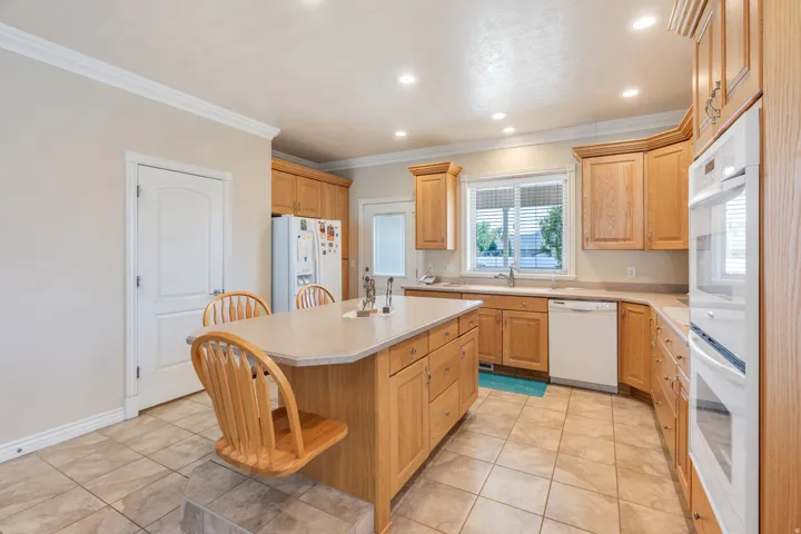 Wood-finish cabinetry with crown molding, a kitchen island with seating, a built-in double oven, recessed lighting, and tile flooring