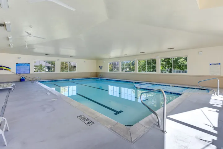Indoor swimming pool with integrated spa, multiple windows, vaulted ceiling, and recessed lighting